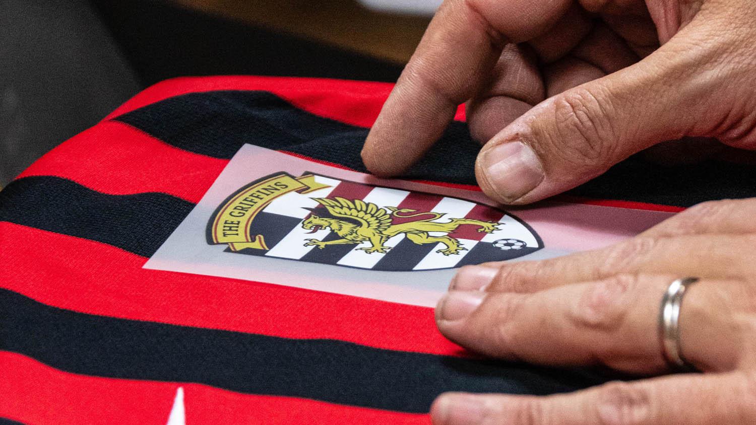 Applicazione a mano di un transfer DTF su maglia sportiva rossa e nera prima della pressatura