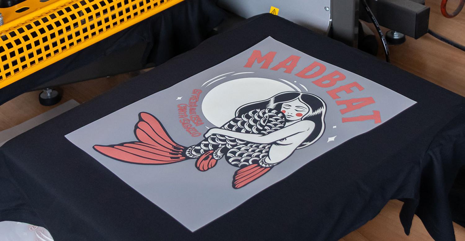 Transfer DTF con illustrazione di sirena su T-shirt nera posizionata su termopressa
